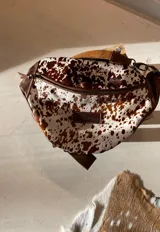 Riñonera de cuero con estampado animal en marrón y blanco, con detalles en cuero marrón liso y correa ajustable.