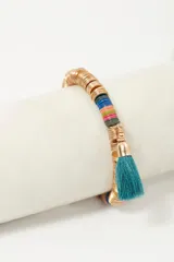 Pulsera elástica con lentejuelas metálicas doradas y plásticas de colores. Incluye borlas de hilo rojas y verde agua.
