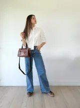 Cartera bandolera de cuero color marrón tostado, con doble asa corta y correa larga desmontable. Tiene un bolsillo frontal con cierre y un bolsillo interno.