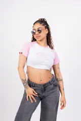 Crop top blanco con mangas cortas raglán color rosa y estampado frontal con texto en rosa.