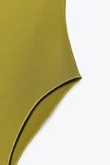 Body bandeau color verde oliva confeccionado en tejido elástico, con escote recto y hombros descubiertos. Cierre inferior con botones a presión.