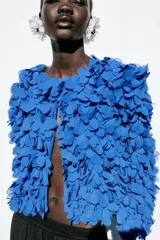 Chaqueta azul con cuello redondo y manga larga, con apliques de pétalos en toda la prenda y cierre frontal con botón a presión oculto.