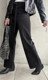 Pantalón de jean negro de corte recto, con tachas plateadas y cinturón fino con hebilla metálica.