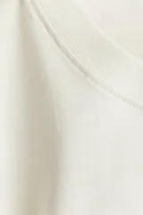 Remera color crema de corte holgado con cuello redondo y hombros caídos. Estampado frontal con la frase "Sans Limites" en color marrón.