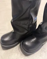 Bota corta negra de estilo motociclista, caña arrugada y suela plataforma gruesa. Presenta tres hebillas metálicas ajustables en el lateral exterior.