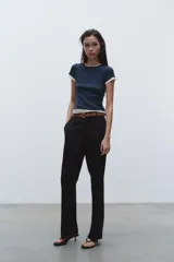 Pantalón negro de tiro alto con pernera recta, bolsillos frontales y falsos bolsillos con solapa en la espalda. Incluye cinturón marrón de cuero sintético.