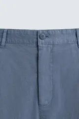Pantalón de hombre color azul grisáceo, estilo balloon fit, confeccionado en mezcla de algodón y lino. Presenta pliegues en el delantero, cierre frontal con botón y cremallera, bolsillos laterales y bolsillos traseros de plastrón.