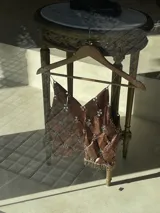 Top de cuero genuino color cobre con acabado metalizado. Presenta un diseño acolchado en forma de rombos, unido con argollas metálicas plateadas con forma de trébol. Tiene tirantes finos de cadena plateada y un borde inferior con flecos de cuentas metálicas doradas.