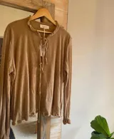 Blusa color marrón claro confeccionada en lino, de manga larga con elástico en los puños, escote en V con doble lazo y corte irregular.