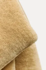 Abrigo largo color camel con efecto piel de oveja, cuello solapa, manga larga, bolsillos delanteros y cinturón ajustable con lazadas. Forro interior.