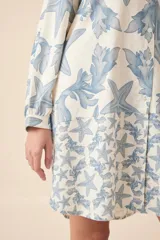 Vestido camisero corto de lino color blanco con estampado de estrellas de mar y algas en azul. Tiene cuello mao, mangas largas y cierre frontal con botones.