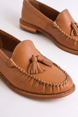 Mocasines de cuero color marrón claro con detalle de borlas en el empeine y costuras decorativas.