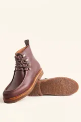 Bota de cuero vacuno color bordó con acabado brillante, diseño tipo botineta con cordones y ganchos metálicos. Presenta suela de goma tipo crepe con plataforma y costuras visibles en la puntera.