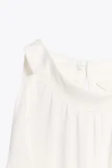 Top blanco sin mangas con cuello halter y volantes en los bordes. Cierre con botón oculto en la espalda.