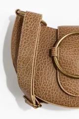 Cartera bandolera marrón con textura símil cuero, correa ajustable, hebilla redonda decorativa y forro de tafeta.