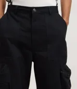 Pantalón masculino de sarga color negro, modelo super baggy con cintura con trabilla, cierre tradicional y bolsillo cargo con cierre de cremallera en el lateral.