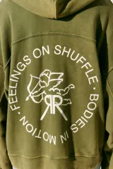 Buzo verde militar de algodón rústico con capucha, corte oversize, cierre metálico, bolsillos delanteros, estampa en frente y espalda, cordón con puntera de goma y lavado acid wash suave.