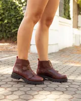 Botinetas de cuero color marrón con suela track negra. Presentan un cierre frontal con detalle en color rojo, dos correas con hebillas metálicas ajustables y puntera redondeada.