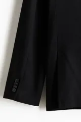 Blazer negro de doble botonadura en tejido suave, con solapas de pico, bolsillo superior, bolsillos ribeteados con solapa adelante y dos bolsillos en el interior. Botones decorativos en los puños y doble abertura atrás. Corte estándar y forro interior.