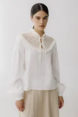 Blusa beige de lino con cuello alto de crochet y mangas largas abullonadas.
