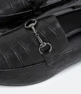 Mocasines negros con textura croco, puntera redondeada y detalle metálico en la parte superior.