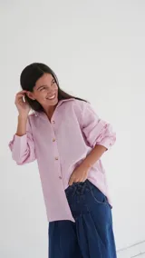 Camisa celeste a rayas verticales blancas, de corte recto, con cuello clásico, cierre frontal con botones y mangas largas con puños abotonados.
