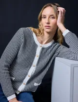 Cardigan de tejido tweed blanco y negro con escote redondo y cierre frontal con botones dorados. Tiene bolsillos simulados en la parte delantera y ribete blanco en cuello, puños y bajo.