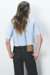 Camisa celeste de popelín con cuello solapa, escote pico y manga corta. Presenta dos bolsillos delanteros de parche y cierre frontal con botones.