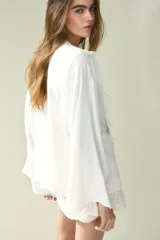 Blusa color crema de crepé de viscosa con mangas largas acampanadas y pechera con volados y bordado floral. Tiene cuello redondo y lazo para atar en el frente.