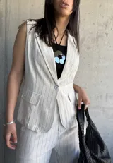 Chaleco sastrero largo color natural con rayas verticales finas. Tiene solapas, bolsillos delanteros y cierre con un botón.