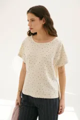 Blusa color crema con estampado de lunares negros, cuello redondo y mangas cortas.