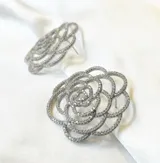 Par de aros rígidos con forma de flor calada, con incrustaciones de circonias.