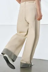 Jeans de tiro medio color beige, corte relaxed leg y largo al tobillo. Cuentan con cinco bolsillos y bajo con vuelta a contraste en gris. Cierre frontal con cremallera y botón.