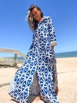 Vestido camisero largo con estampado geométrico azul y blanco, cuello camisero, mangas largas con puños y abotonadura frontal. Presenta aberturas laterales en el ruedo.