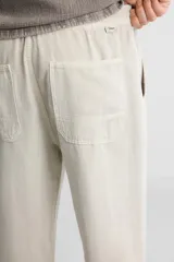 Pantalón color arena de corte recto, confeccionado en tejido de algodón y lino. Cuenta con cintura elástica ajustable con cordón, bolsillos delanteros y traseros de parche.