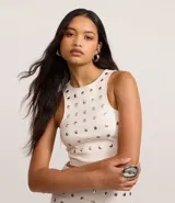 Top cropped sin mangas, color blanco, con escote redondo y tachuelas metalizadas distribuidas por toda la prenda. Posee cierre lateral de cremallera.