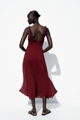 Vestido midi color borgoña con escote en V, tirantes anchos con detalle de nudo y falda plisada. Cierre trasero con cremallera oculta.