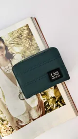 Billetera corta con cierre alrededor y tapa, confeccionada en tela capitoneada. Incluye varias reparticiones con tarjeteros y bolsillos internos, y una correa de mano desmontable. Disponible en negro, rojo y dorado.