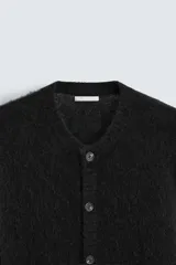 Cárdigan negro de punto con textura, corte regular, cuello redondo, manga larga, terminaciones en rib y cierre frontal con botones.