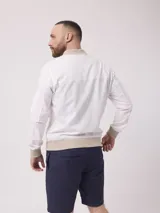 Campera bomber color blanco confeccionada en lino y algodón, con cuello mao, cierre frontal con cremallera, bolsillos frontales con cierre y puños y ruedo acanalados en color beige.