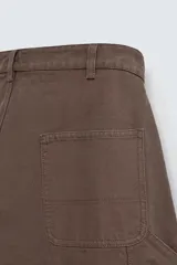 Pantalón negro de corte amplio, confeccionado en tejido de algodón con efecto lavado. Presenta bolsillos frontales, traseros de parche, tira multifunción y bolsillos laterales en las perneras. Cuenta con cierre frontal con cremallera y botón.