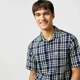 Camisa de manga corta a cuadros azules y blancos, con cuello clásico y bolsillo en el pecho.