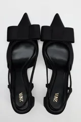 Zapato destalonado negro con tacón ancho y tira trasera. Detalle de lazo en la parte delantera.
