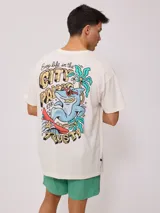Remera color crema de algodón con estampado en la espalda de un tiburón con gafas de sol, palmeras y texto "Easy life in the City of Palm Rusty 1985".