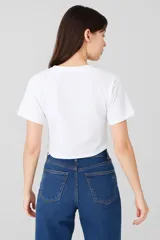 Remera cropped negra de algodón con cuello redondo y estampado de hojas blancas en el hombro.