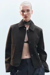 Chaqueta corta negra de cuello solapa y manga larga con puños. Tiene bolsillos de parche en el frente y cierre frontal con botones.