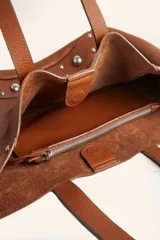Bolso tote de cuero color marrón con tachas plateadas en los laterales. Tiene doble asa de hombro y un sobre interior de cuero.