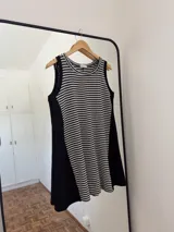 Vestido corto sin mangas, de silueta amplia y calce relajado. El frente es de tejido a rayas horizontales blancas y negras, mientras que los laterales son lisos en color negro. Posee escote redondo.