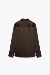Camisa de mujer satinada color blanco, confeccionada en hilatura con viscosa. Tiene cuello solapa, manga larga con puños y cierre frontal con botones.