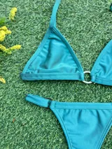 Bikini de dos piezas color celeste metalizado, compuesto por un corpiño triangular con argolla central de zamak y una bombacha colaless con argollas ajustables en los laterales. Incluye copas soft removibles.